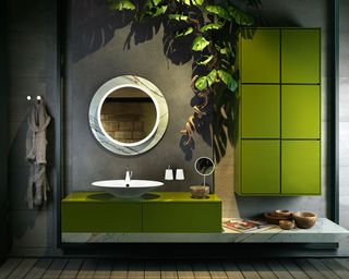 A dark green bathroom trend with green units, round mirror and plants.
