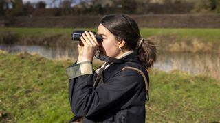 A female photographer holds the Camonity 5M 2" LCD 16GB Digital Binoculars in her hands in a sunny field