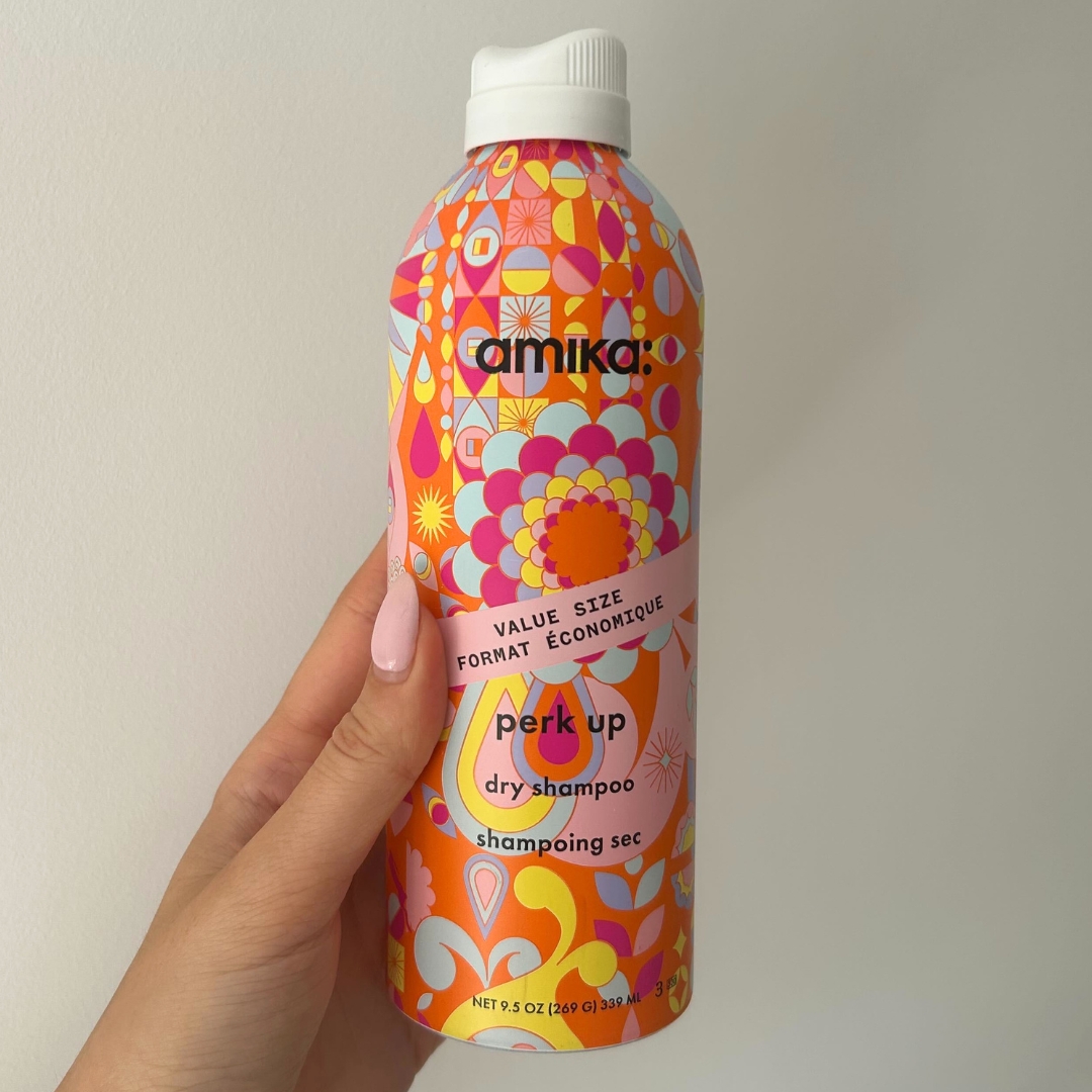 Hand holding empty aerosol of Amika Perk Up Dry Shampoo