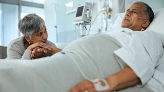 Man in hospital bed with woman holding his hand by his side
