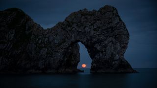 Moonrise through the natural arch of Durdle Door in Dorset, UK.