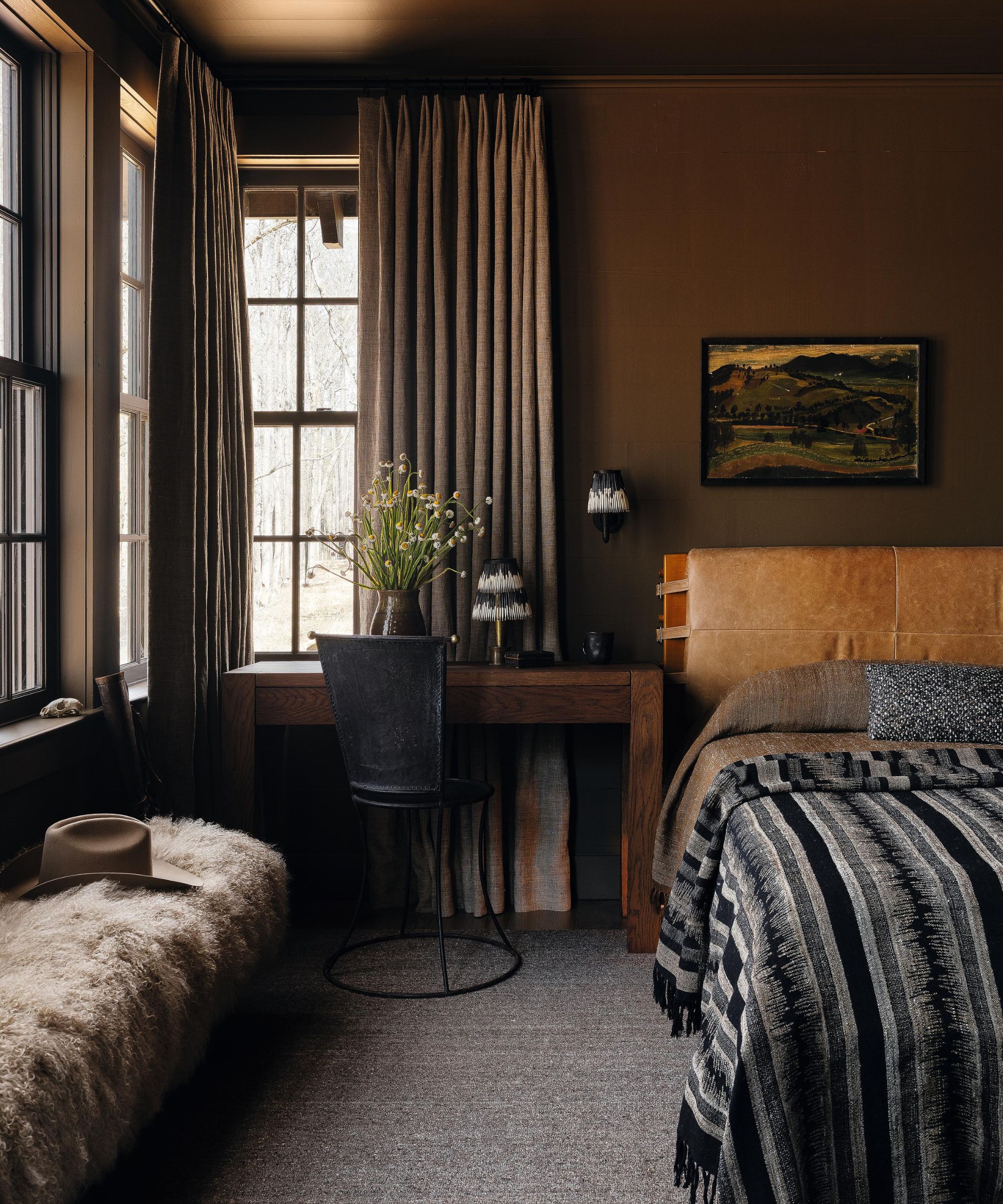a moody brown bedroom with a leather headboard and rustic textured bed linen