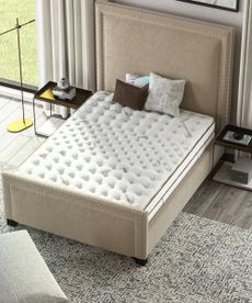 Bird's eye view of Saatva Latex Hybrid on a beige bed frame on a gray carpet with a dark wood nightstand either side. 