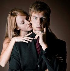 man in suit with woman behind him nuzzling his neck