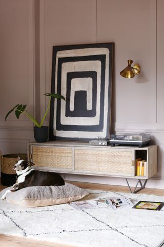 pink living room with wood sideboard and artwork, record player and brass wall light, patterned rug