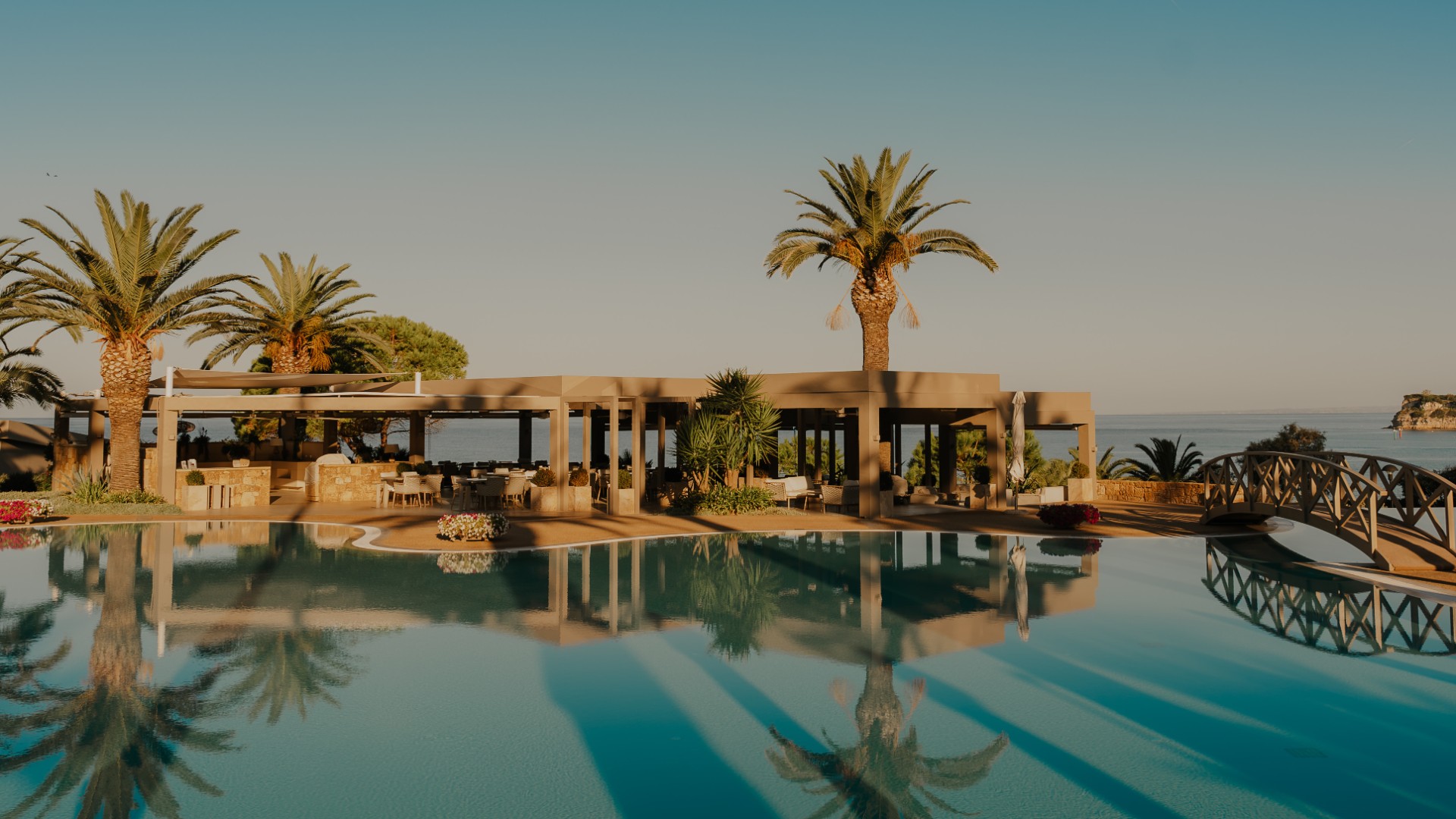The Sani Club swimming pool, showing palm trees in the background a small bridge over the water