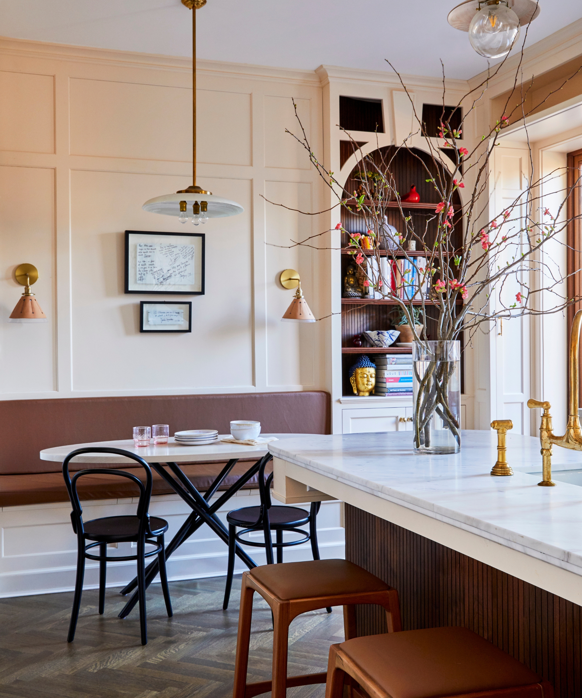 The corner of a pale pink kitchen with an arched shelving unit and a brown banquette dining nook