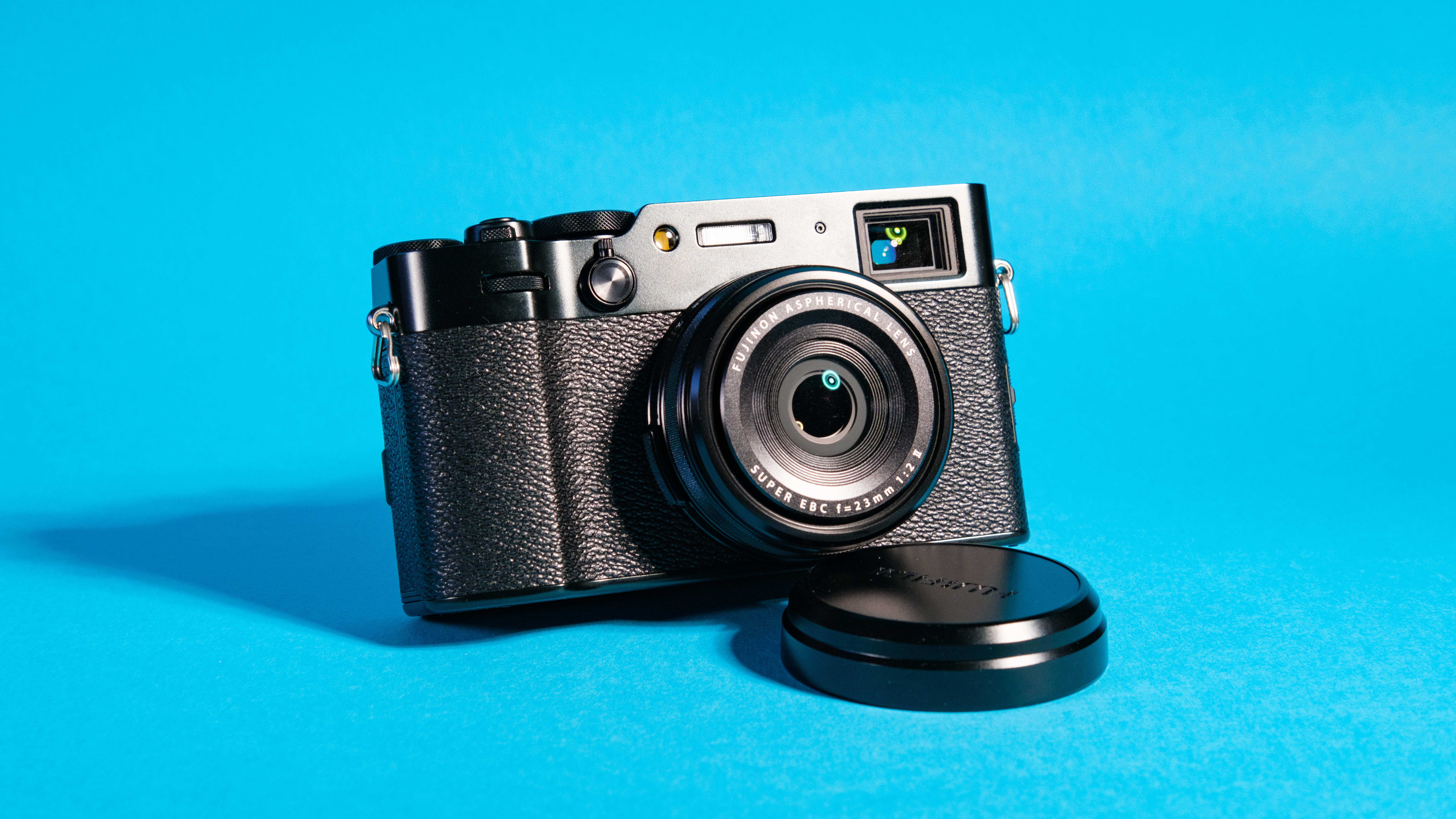 The Fujifilm X100VI mirrorless camera against a blue background propped up using the lens cap.