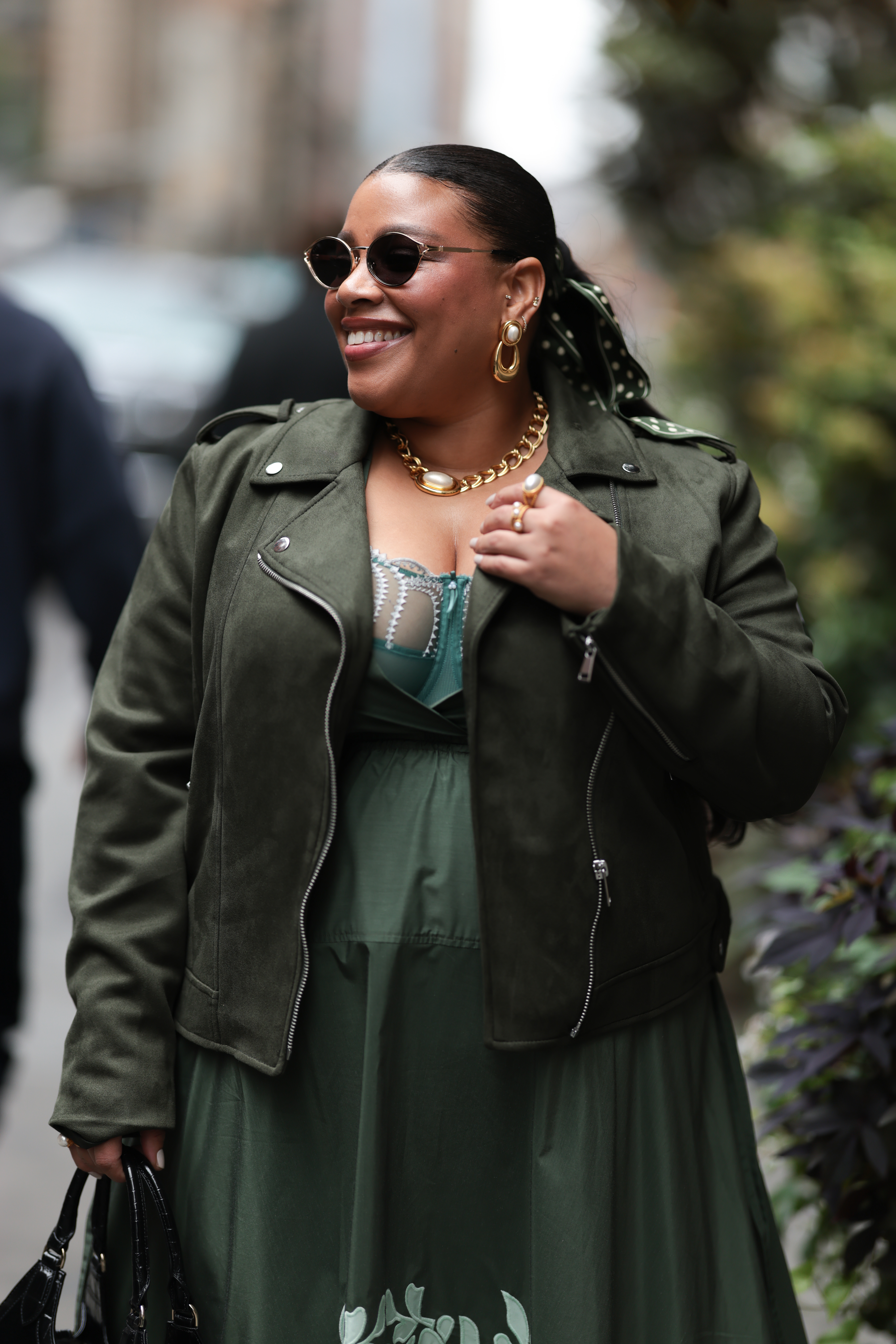 a woman wearing a green dress and green leather jacket with a long dark ponytail during new york fashion week