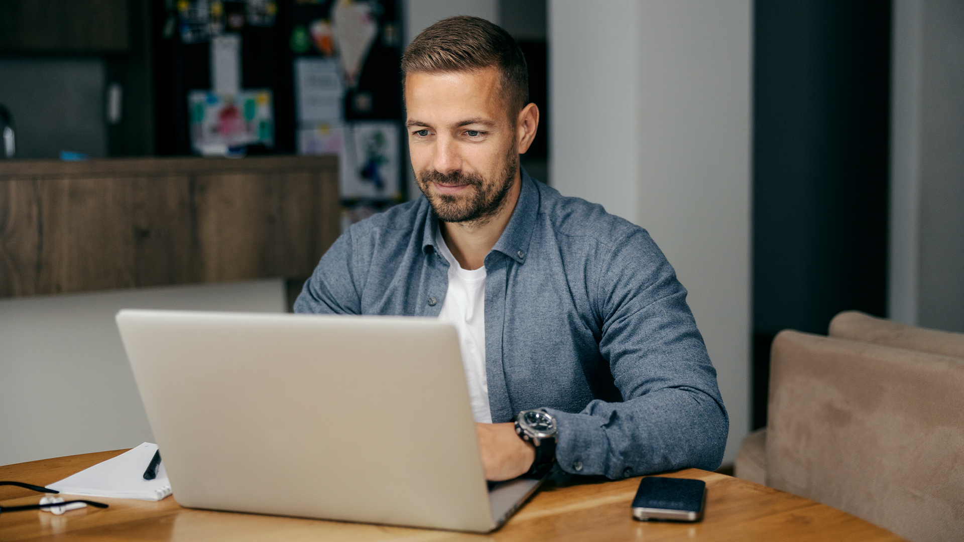 A man smiles as he sits at the desk, using his laptop