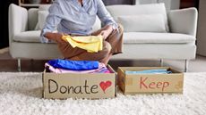 A woman folds a shirt while sitting on the sofa behind boxes marked "donate" and "keep."