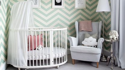 Nursery with green and white zig zag wallpaper and white oval cot