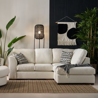 A living room with a corner cream sofa, a jute rug and a panelled wall section in black