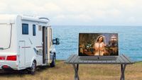 A medium shot of a caravan overlooking the ocean. The 24MPE7002Z TV is on a table facing away from the sea.
