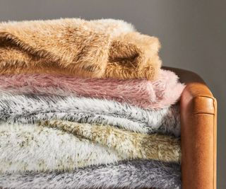 A pile of folded fluffy blankets, folded up on top of a wooden armed chair.