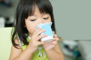 A young girl eating yogurt out of a cup.
