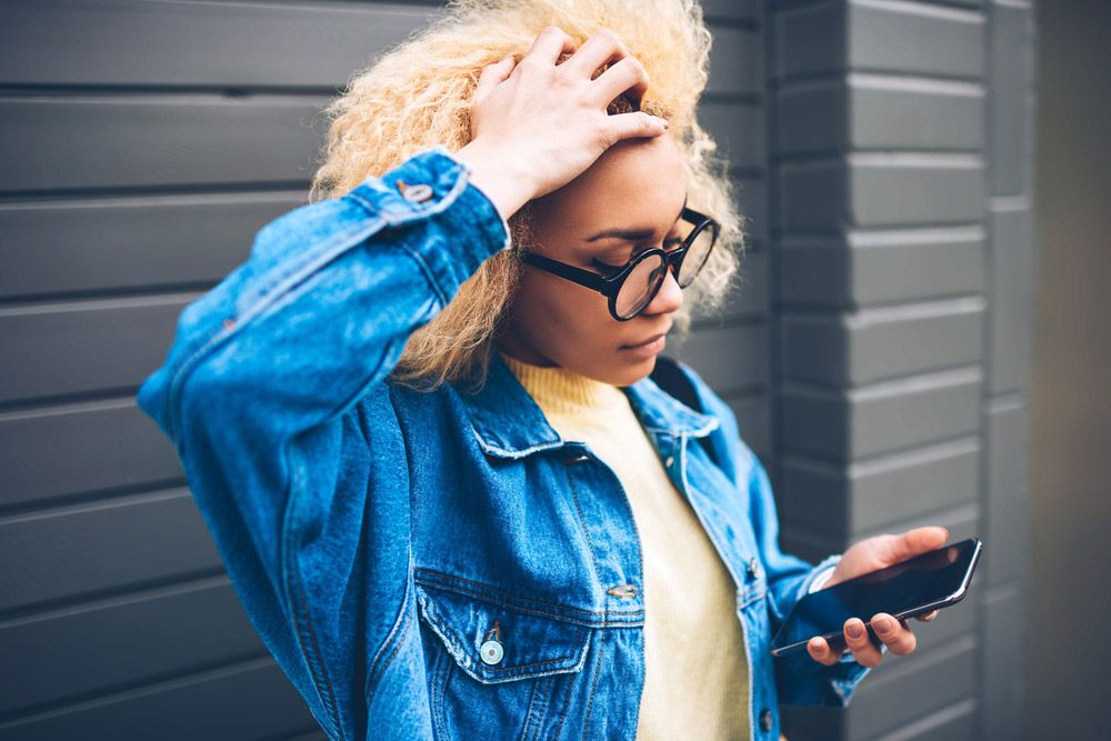 Young woman looking at phone and grasping hair in frustration.