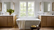 A large bathroom with walls painted Swiss Coffee by Benjamin Moore, two wooden vanities, and a freestanding bath beneath the window