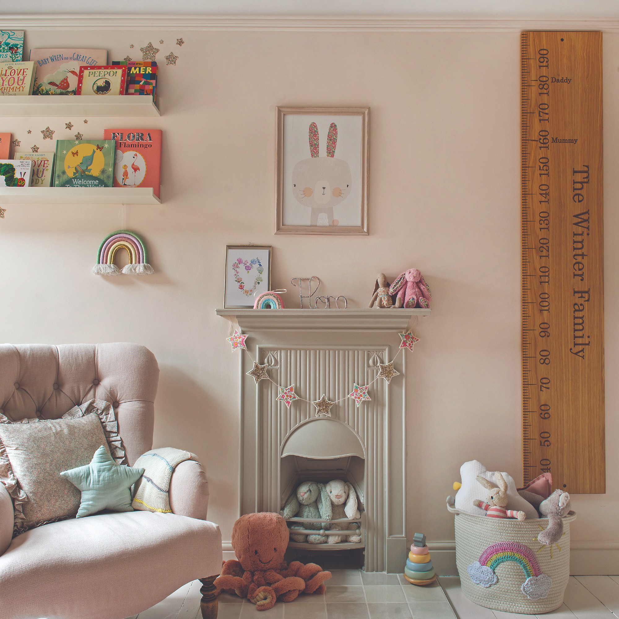 A pink-painted nursery with a pink armchair and a cream fireplace