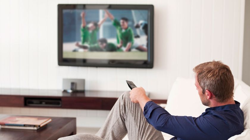 A man watching a TV with a remote control in his hand.