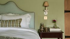 pale green country bedroom with an upholstered headboard, ruffled white bedding and a cute wall sconce