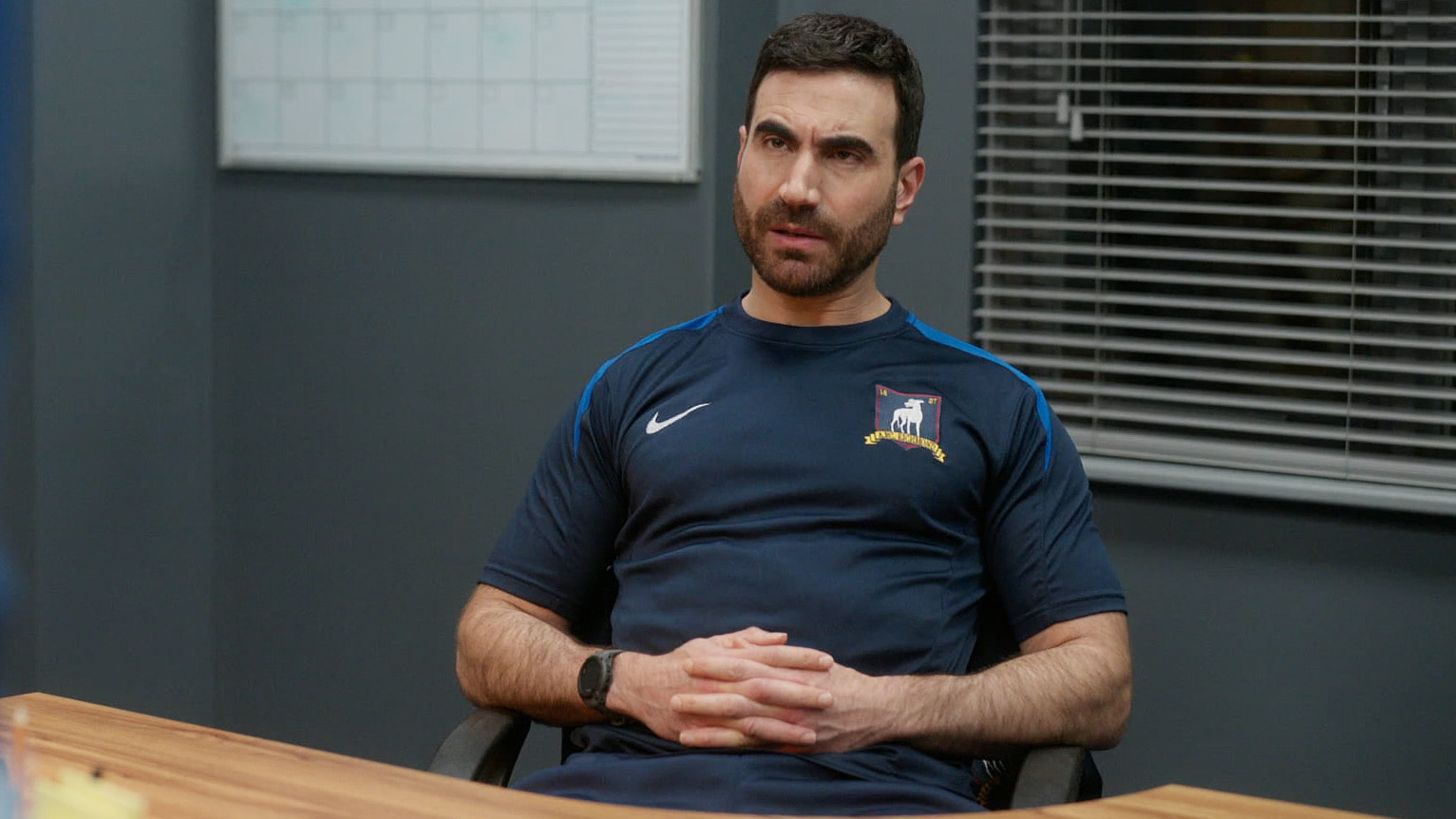 Brett Goldstein's Roy Kent sitting at a desk with hands clasped in Ted Lasso season 4
