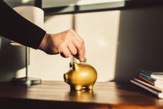 Woman putting coin into a golden piggy bank.