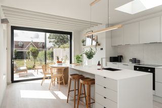 A light kitchen extension with white fittings and a garden beyond the bi-fold doors