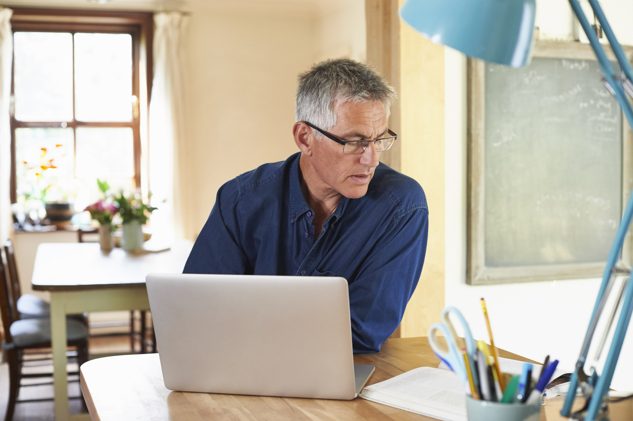 A man in his 50s or early 60s works on a laptop in his home office.