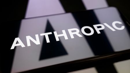 Logo of AI company Anthropic pictured on a smartphone screen placed on top of reflective surface, with company logo reflected.