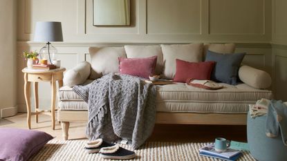 The LOAF Parley day bed in a light beige bisvuit color, styled with a loose throw blanket, pillows, and some life bits such as a magazine and cup of coffee