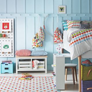 A light blue children's room with wall panelling and multipurpose toy storage solutions