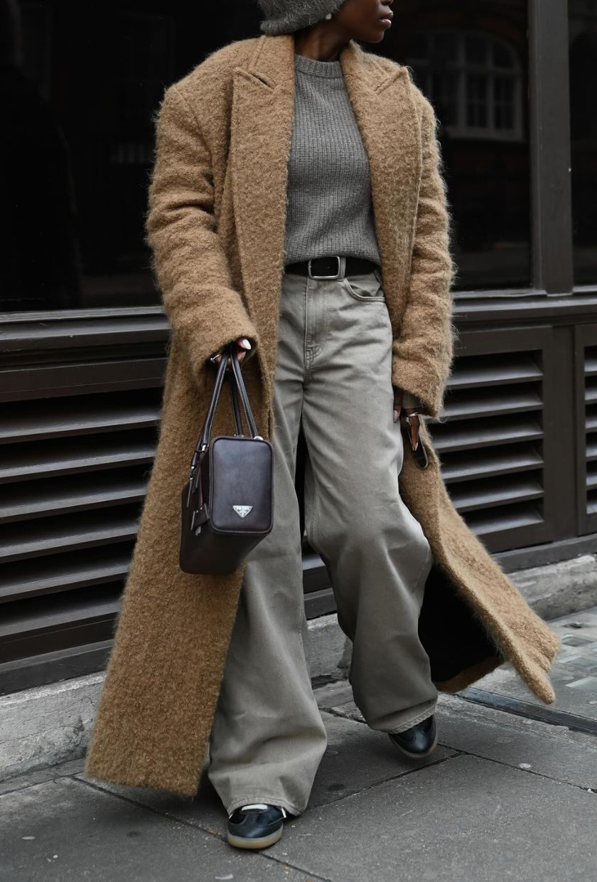 @daniellejinadu wears grey baggy jeans with a tan long coat, grey jumper, black trainers and black bag