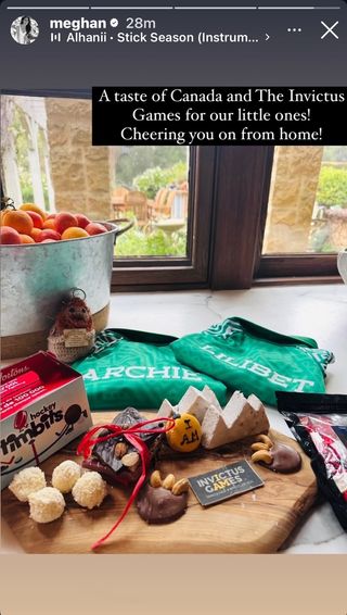 A photo of a wooden cutting board covered in candy and donuts next to green shirts that say Archie and Lilibet and a tin bucket filled with fruit