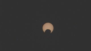 A blurry photo of Mars&#039; moon Phobos passing in front of the sun in a partial eclipse