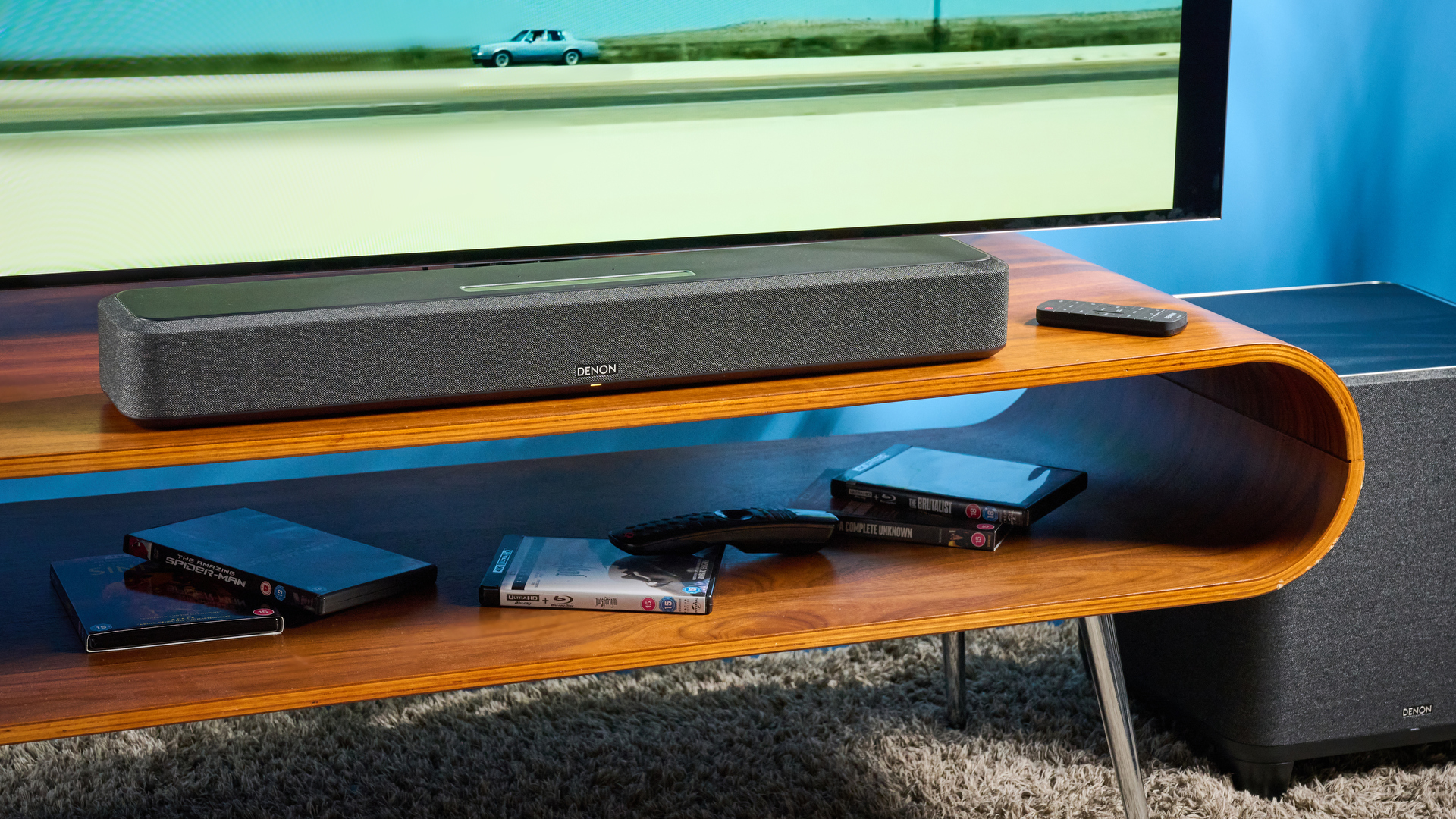 the denon home sound bar 550 with a gray mesh casing and touch controls for bluetooth on the top with a remote and smart home integration