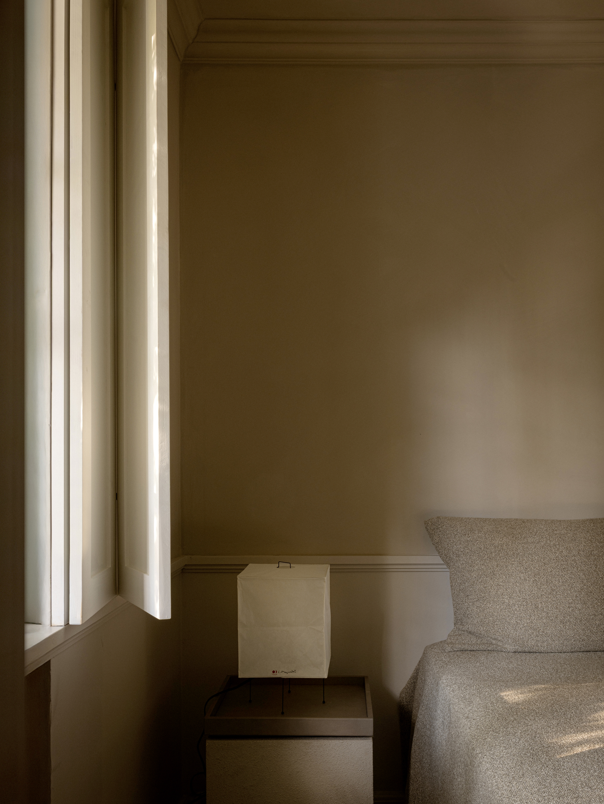 Image of a minimalist, calming bedroom with an all-beige color scheme. There is bed with no headboard, and side table with a small paper lantern.