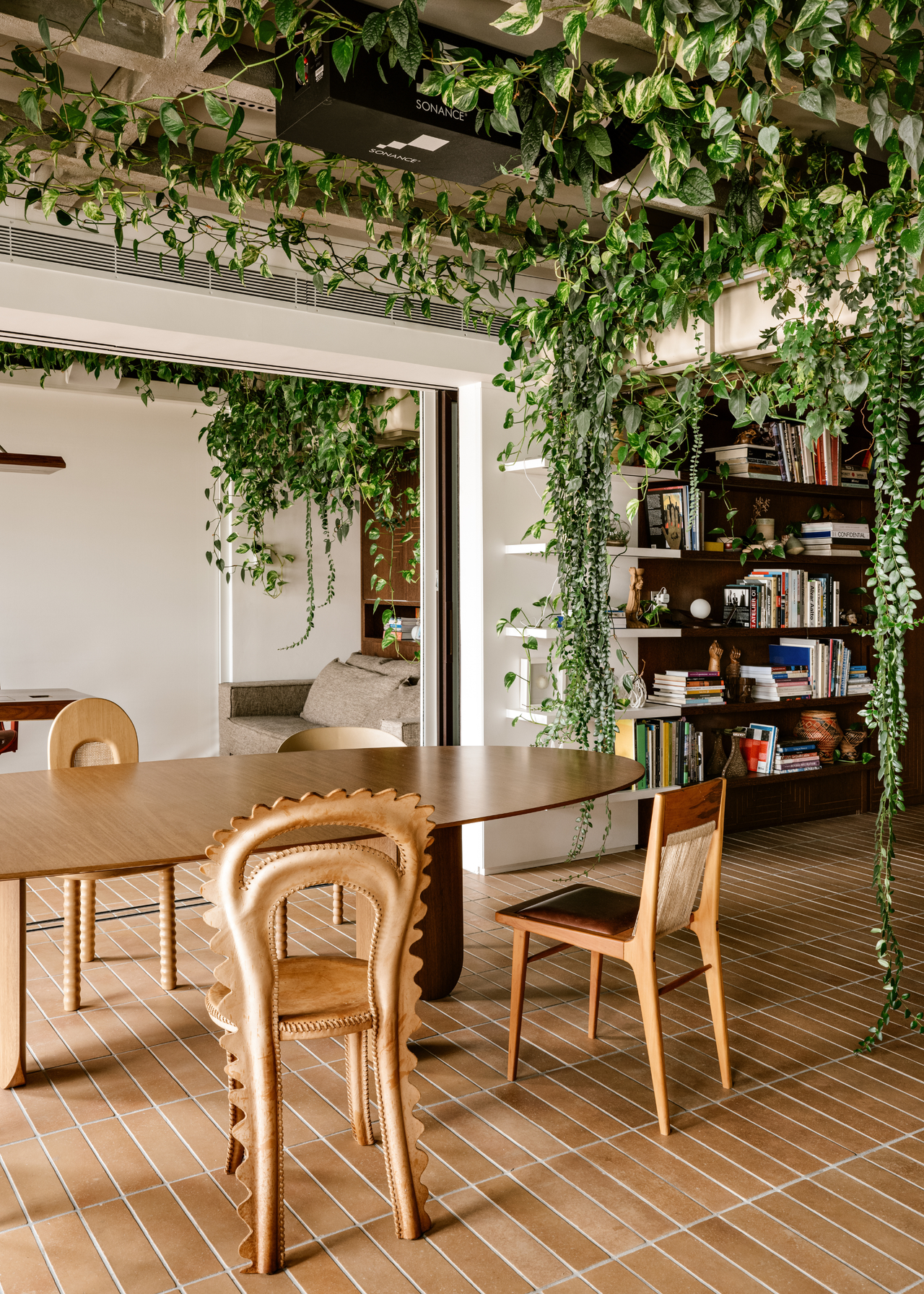 An open-concept dining room with mismatched chairs and verdant foliage above
