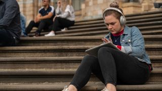 A young woman sitting on steps wearing headphones and using a laptop