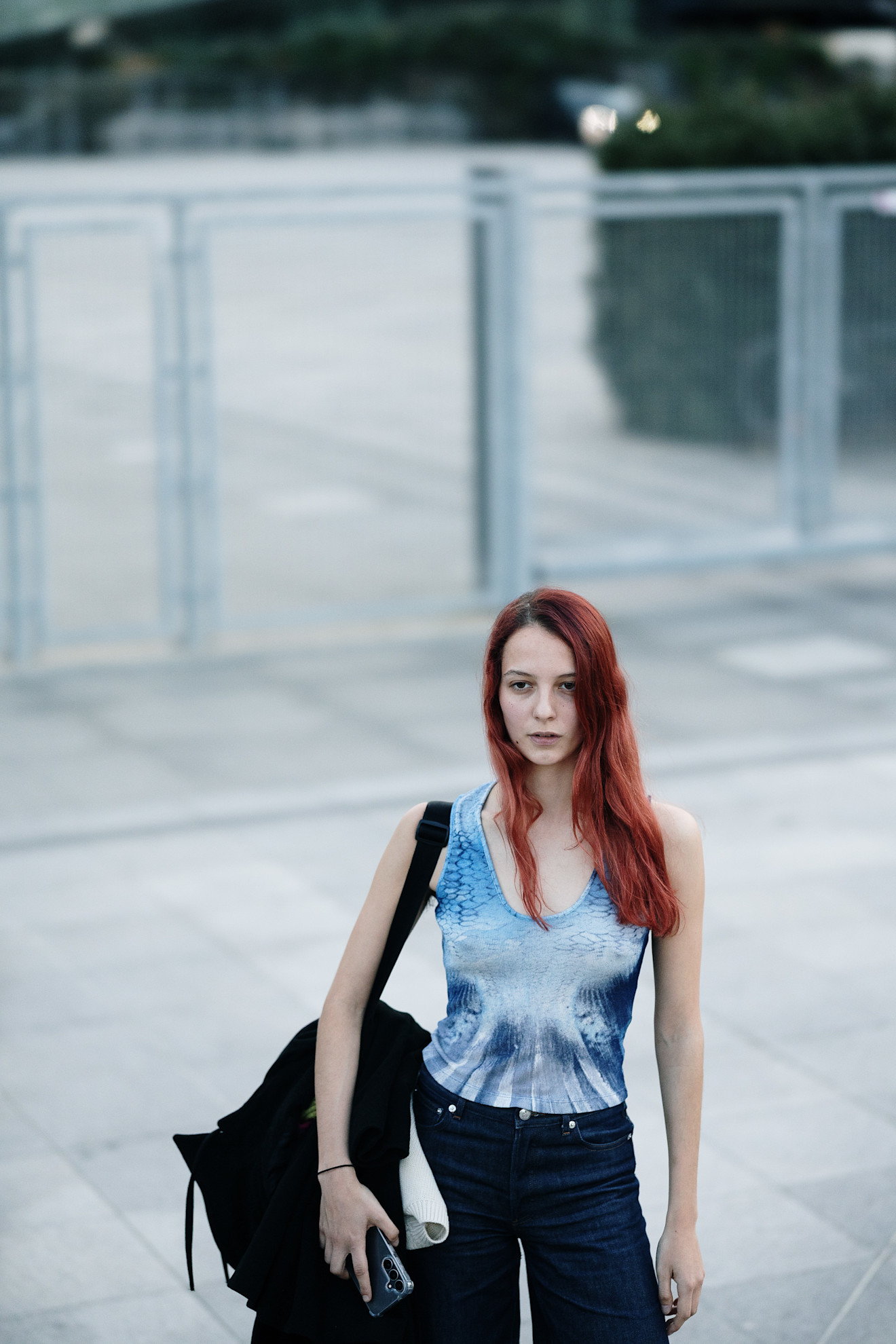 a woman with red hair in a blue tank top and black pants