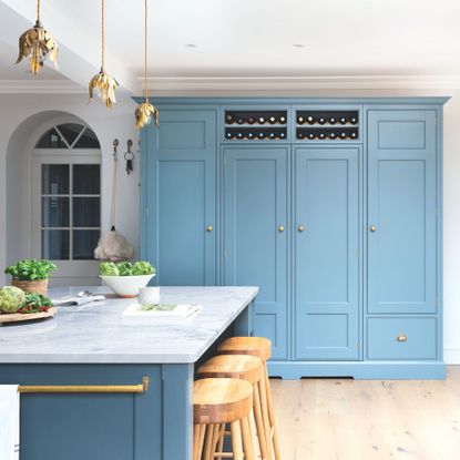 Kitchen with pastel blue storage at the back of the room and a blue kitchen island with marble worktop