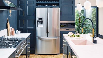 Blue kitchen with gold hardware, wooden parquet floor and silver fridge freezer