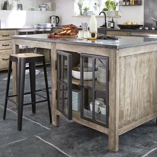 semi-portable wooden kitchen island with black top and glass cupboard, with stool and seating area, in a kitchen with black floor slabs