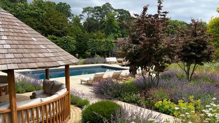 A garden with flower beds, a pool, and a pergola over garden seating