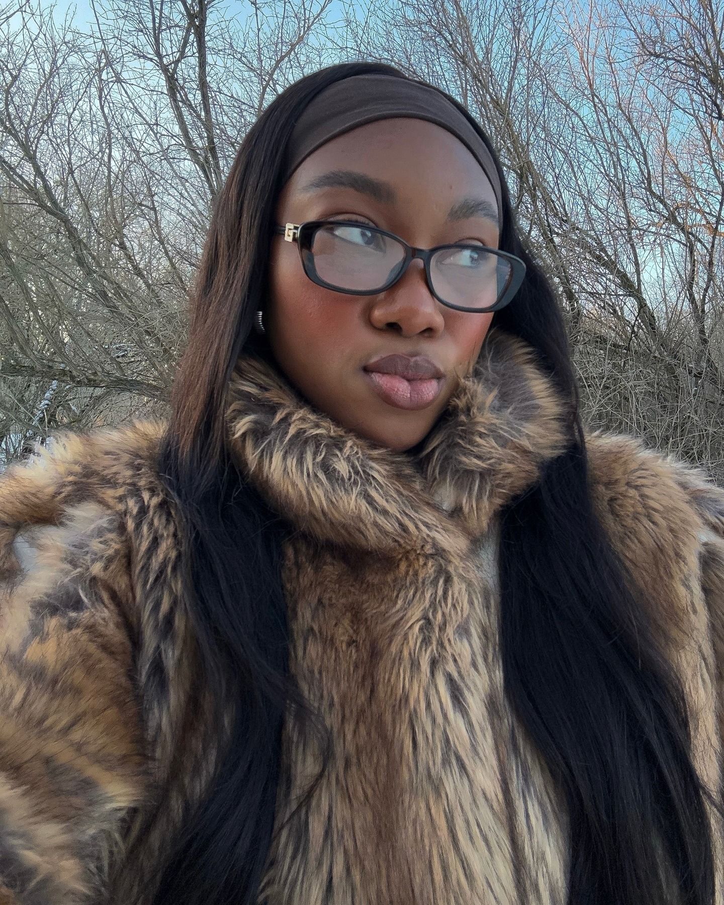 A woman taking a selfie wearing a fur coat and a thick headband