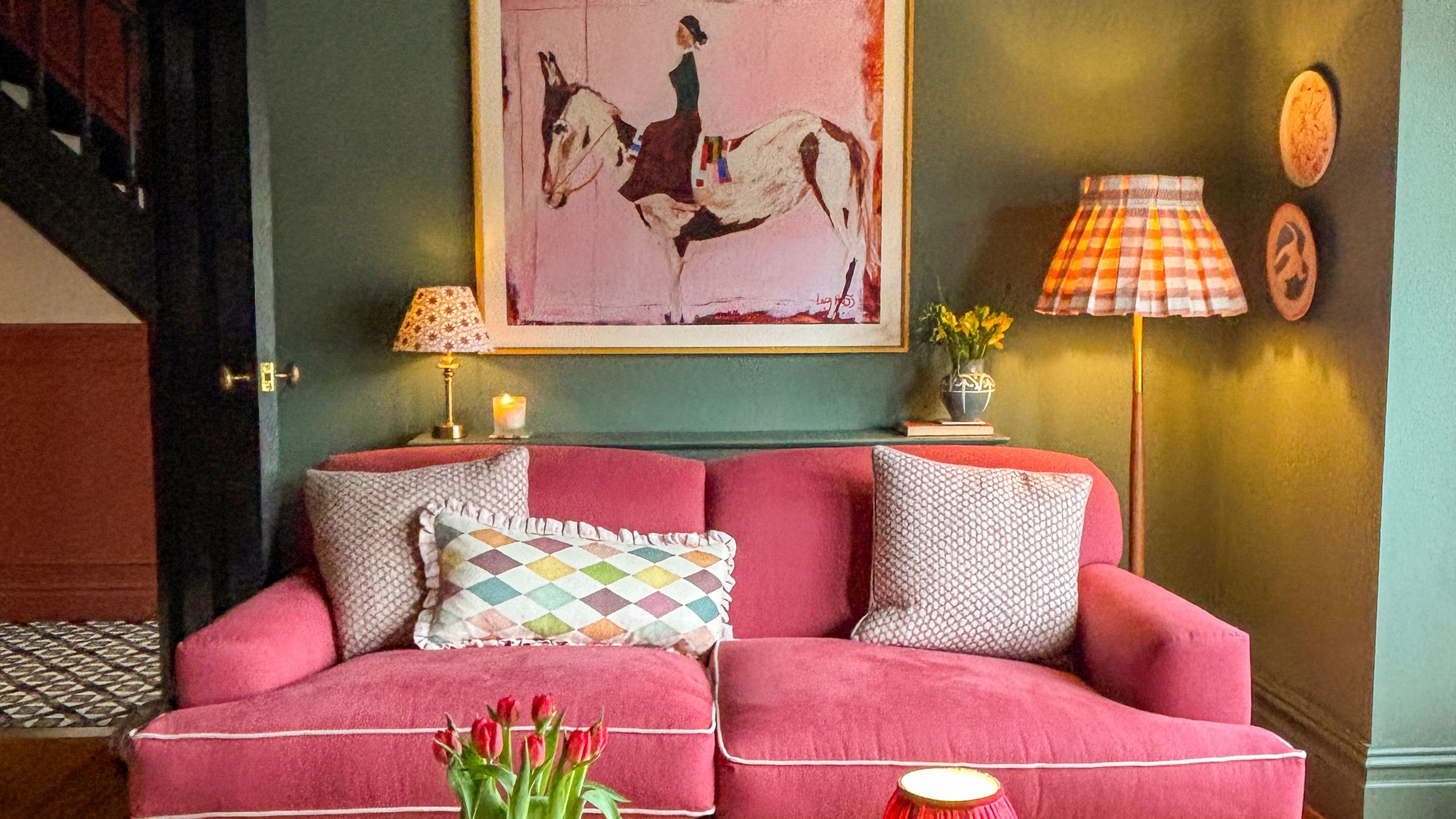 Green living room with pink sofa, pink painting with horse and floor lamp with striped fabric shade