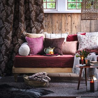 iving room or cosy snug, sofa with multiple cushions and throws, leaded window, wooden floor and rug. Autumnal warm natural colours.
