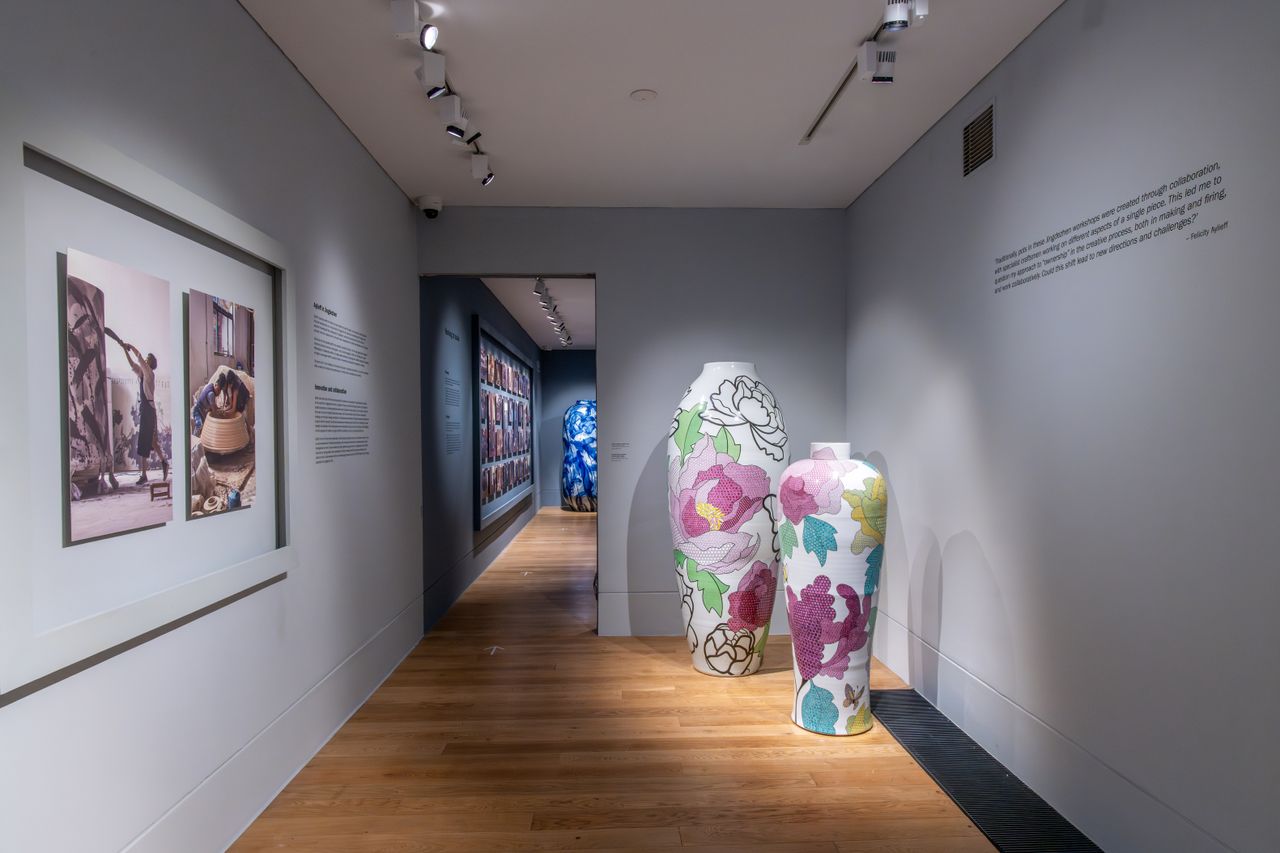 A series of gigantic china-style vases is on display in a warmly lit gallery, including some blue and white pieces and some more widely colored ones.