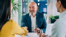 A financial adviser smiles as he shakes the hand of a client in his office.