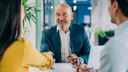 A financial adviser smiles as he shakes the hand of a client in his office.